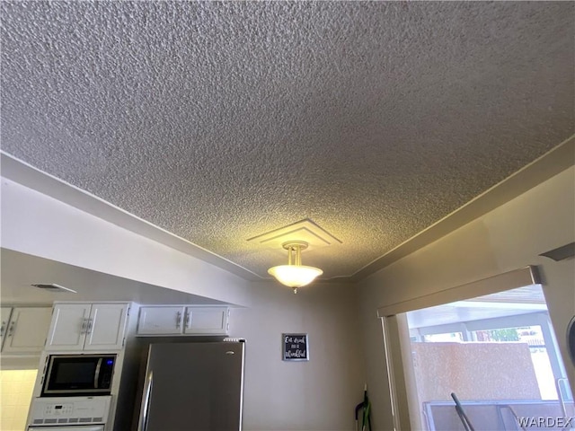 room details with wall oven, visible vents, white cabinets, freestanding refrigerator, and a textured ceiling