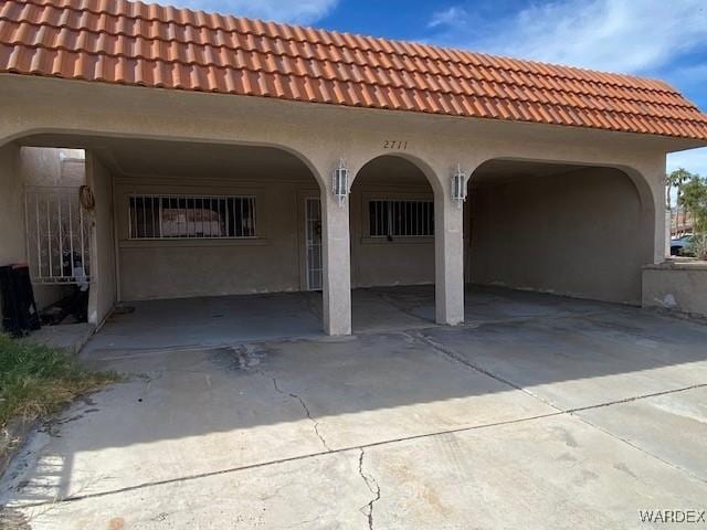 rear view of property with concrete driveway, an attached carport, and stucco siding