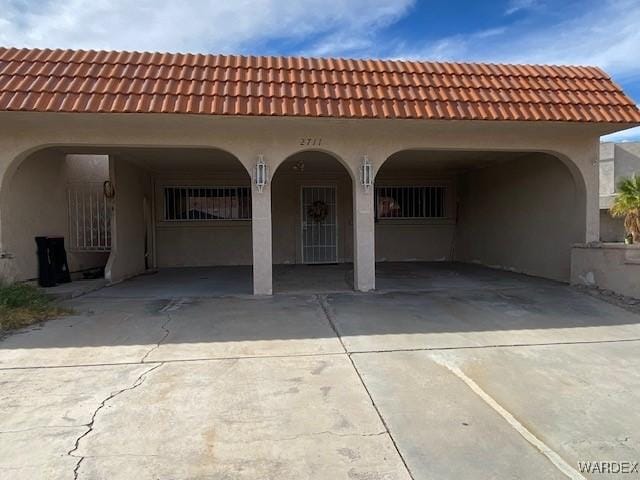 back of house featuring a tile roof, concrete driveway, and stucco siding