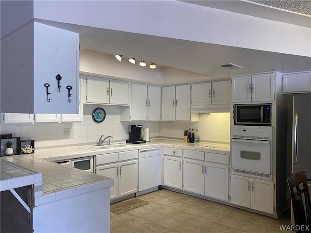 kitchen with tile counters, decorative backsplash, appliances with stainless steel finishes, white cabinetry, and a sink