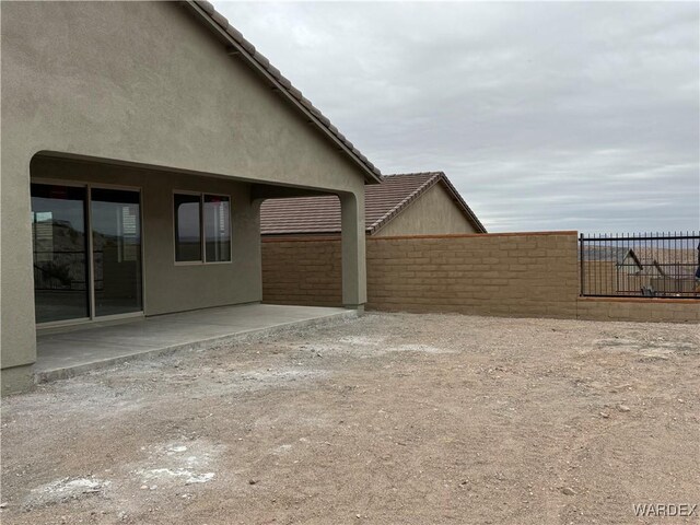 view of side of home featuring a tile roof, fence, a patio, and stucco siding