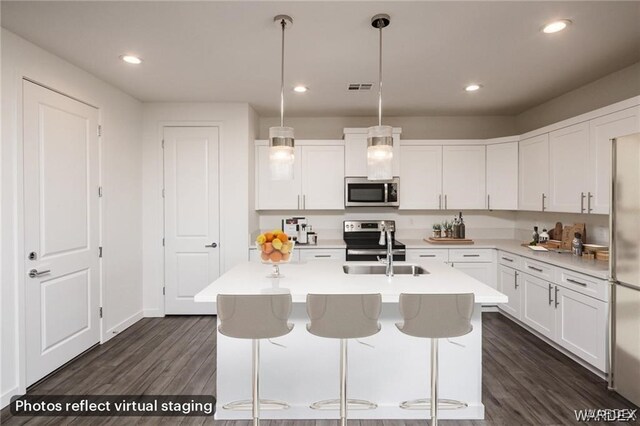 kitchen featuring pendant lighting, stainless steel appliances, light countertops, white cabinetry, and an island with sink