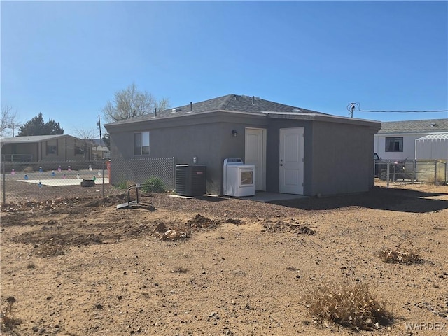 rear view of house with washer / dryer, cooling unit, fence, and stucco siding