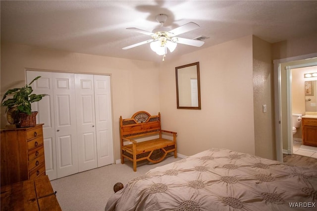 carpeted bedroom with a closet, visible vents, a ceiling fan, ensuite bath, and baseboards