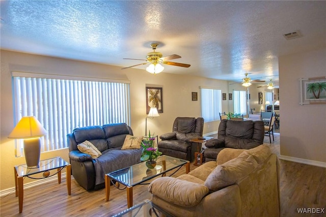 living area featuring a textured ceiling, wood finished floors, visible vents, and baseboards