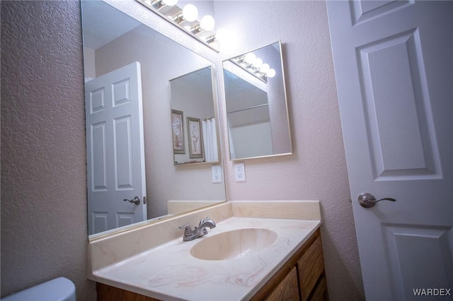 bathroom featuring toilet, a textured wall, and vanity