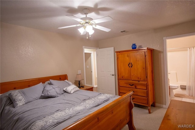 bedroom with ceiling fan, light carpet, visible vents, baseboards, and ensuite bath