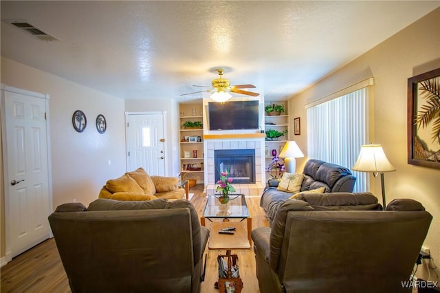 living room featuring a wealth of natural light, visible vents, a tiled fireplace, and wood finished floors