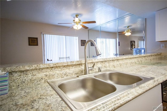 kitchen with a ceiling fan, white cabinets, a sink, and light stone countertops