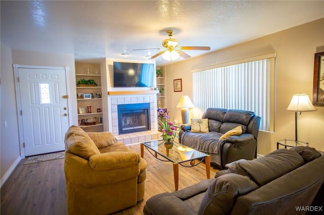 living room featuring a textured ceiling, built in shelves, a fireplace, wood finished floors, and a ceiling fan