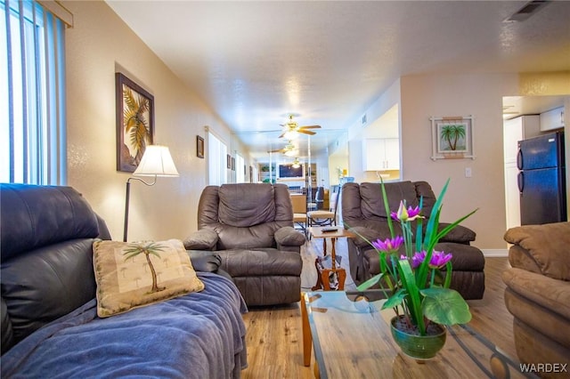 living room featuring a ceiling fan, visible vents, light wood-style flooring, and baseboards