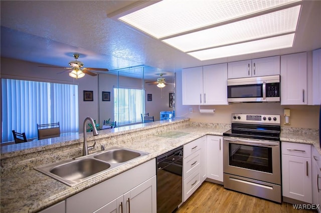 kitchen featuring stainless steel appliances, light wood-style floors, white cabinetry, a sink, and a peninsula