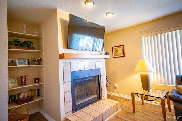 living room with a textured ceiling, a tile fireplace, built in features, baseboards, and light wood finished floors