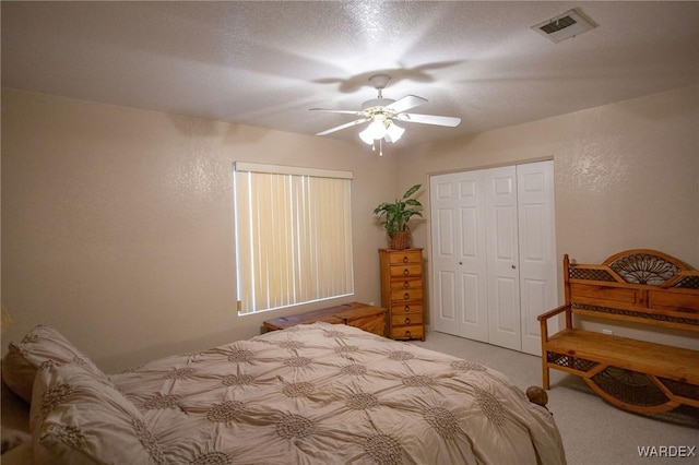 carpeted bedroom with ceiling fan, a textured wall, a textured ceiling, visible vents, and a closet