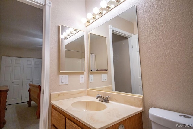 full bathroom with toilet, a textured wall, curtained shower, and vanity