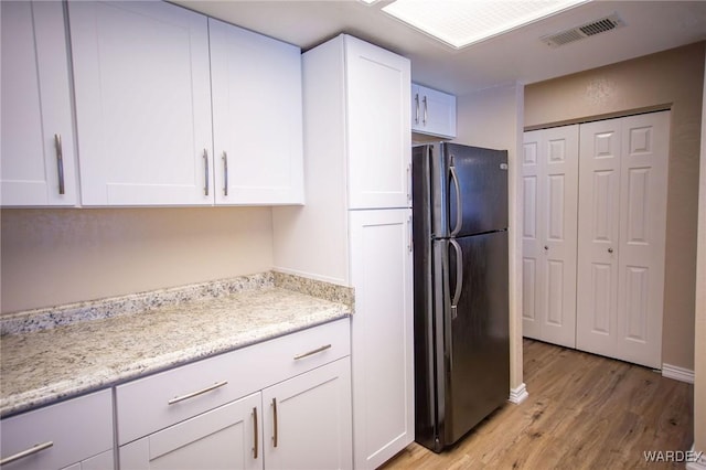 kitchen with light wood finished floors, visible vents, light stone counters, freestanding refrigerator, and white cabinetry