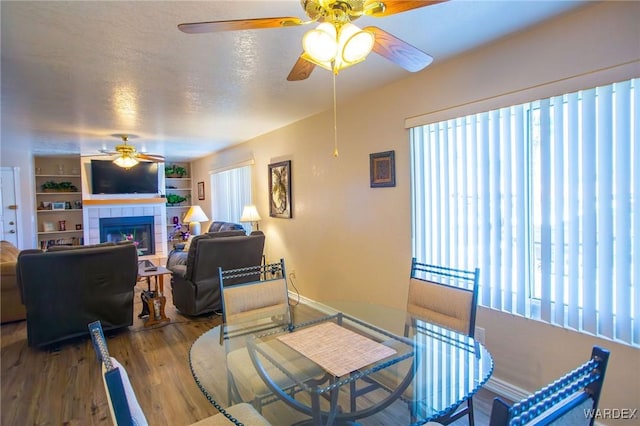 dining space with a healthy amount of sunlight, a textured ceiling, a tiled fireplace, and wood finished floors