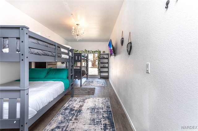 bedroom with baseboards, wood finished floors, an inviting chandelier, and a textured wall