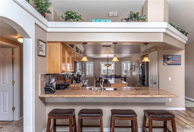 kitchen featuring a peninsula, visible vents, wood finished floors, a breakfast bar area, and baseboards
