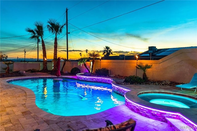 pool at dusk with a fenced backyard, a fenced in pool, an in ground hot tub, and a patio area