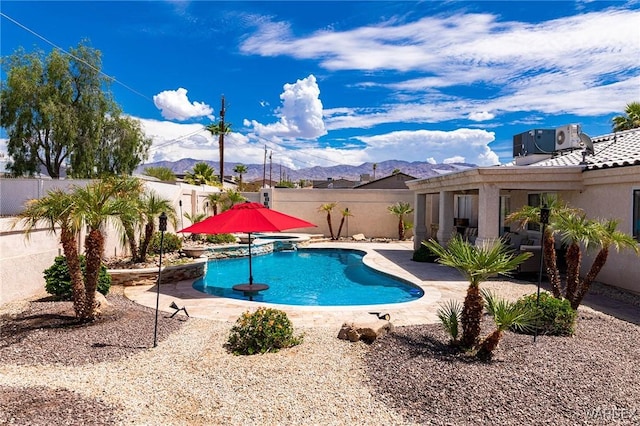 view of pool featuring central AC unit, a mountain view, a patio area, a pool with connected hot tub, and a fenced backyard