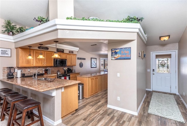 kitchen with tasteful backsplash, appliances with stainless steel finishes, a kitchen bar, a peninsula, and light wood finished floors