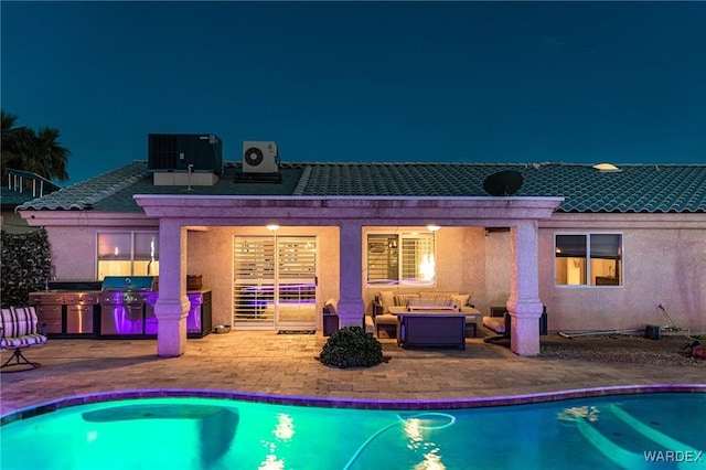 back of house at night featuring central AC, outdoor lounge area, stucco siding, a patio, and an outdoor pool