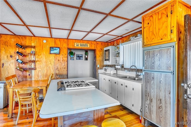 kitchen featuring light countertops, stovetop, light wood-type flooring, open shelves, and a sink