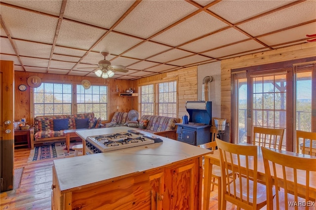 kitchen featuring light wood finished floors, a ceiling fan, a wood stove, open floor plan, and wooden walls