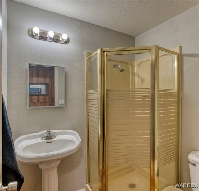 full bathroom featuring toilet, a stall shower, a textured ceiling, and a textured wall