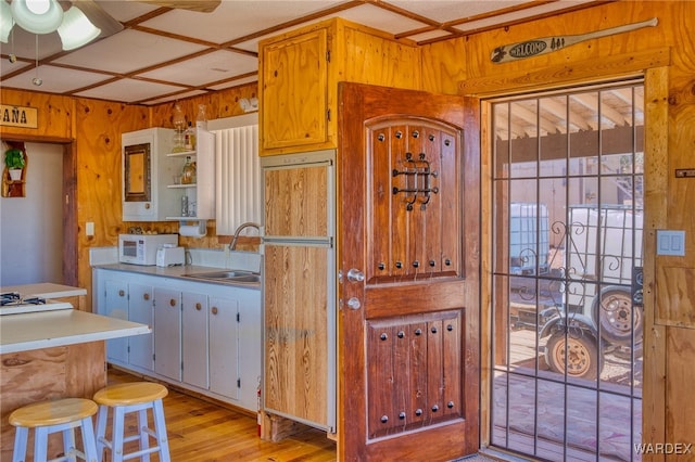 kitchen featuring white microwave, light wood-style flooring, wood walls, open shelves, and a sink