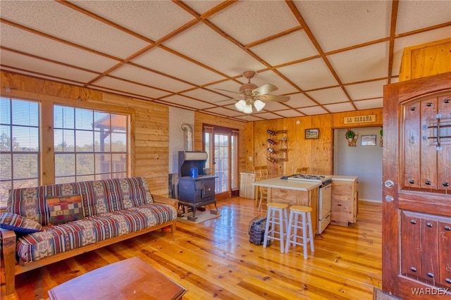 living room with light wood-type flooring, a wood stove, coffered ceiling, and wood walls