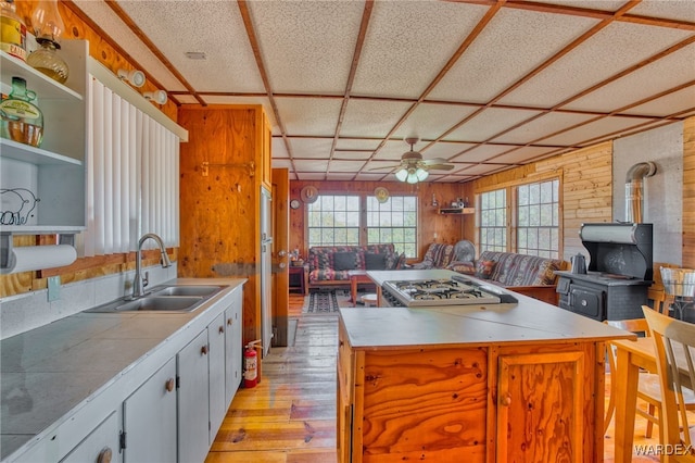 kitchen featuring wooden walls, a sink, a ceiling fan, light wood-style floors, and open floor plan