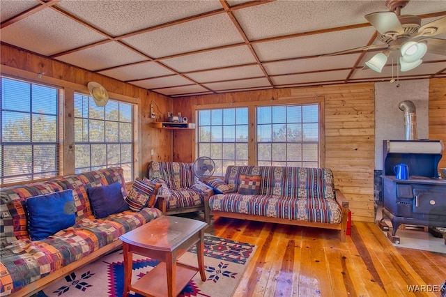 living room with plenty of natural light, a wood stove, wood walls, and hardwood / wood-style flooring