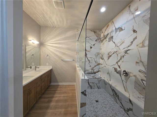 bathroom with double vanity, a marble finish shower, visible vents, wood finished floors, and a sink