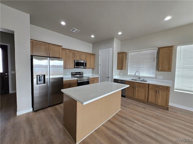 kitchen with a sink, stainless steel appliances, a kitchen island, and light countertops