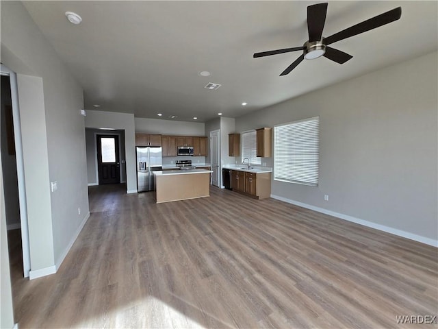 kitchen featuring a center island, light countertops, appliances with stainless steel finishes, brown cabinetry, and open floor plan