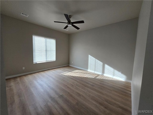 unfurnished room with ceiling fan, wood finished floors, visible vents, and baseboards