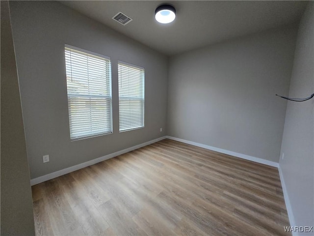 empty room with wood finished floors, visible vents, and baseboards