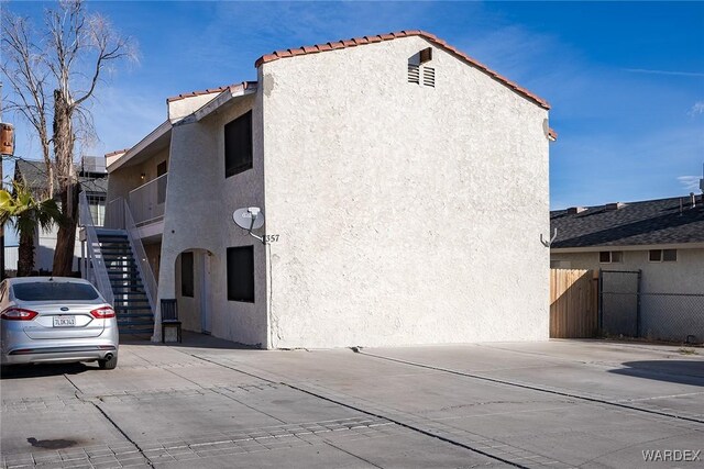 view of side of property featuring a tile roof, fence, stairway, and stucco siding