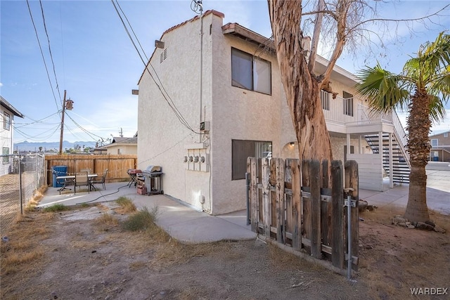 rear view of house featuring a patio, stairway, fence, and stucco siding