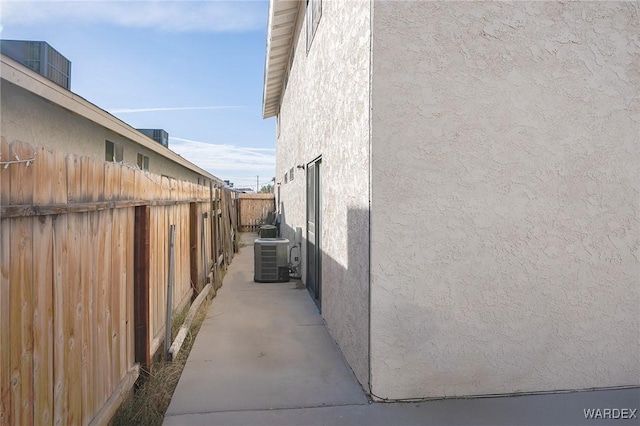 view of side of property featuring fence, central AC unit, and stucco siding