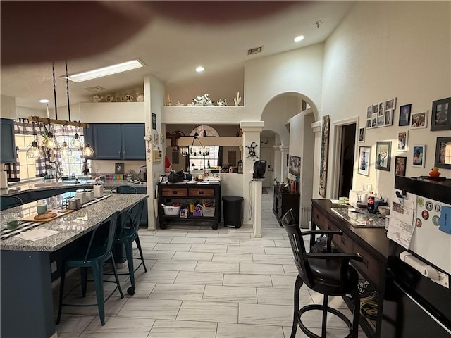 3483 Via Los Pozos, Bullhead City, AZ 86442 - kitchen with arched walkways, light stone countertops, ornate columns, high vaulted ceiling, and a breakfast bar area
