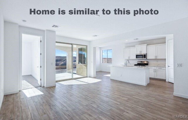 kitchen with a center island with sink, visible vents, stainless steel appliances, light countertops, and white cabinetry