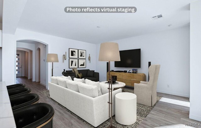 living room with arched walkways, visible vents, baseboards, and wood finished floors