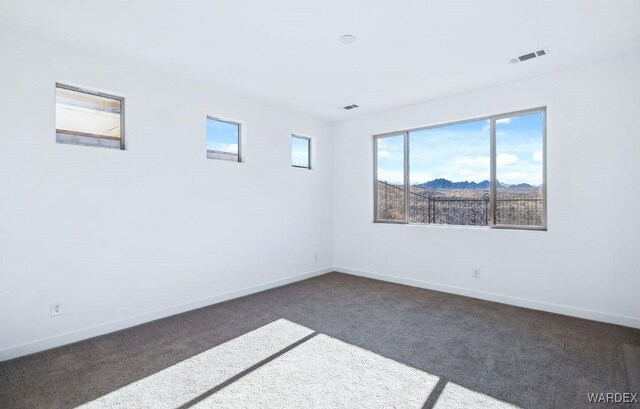 spare room featuring dark colored carpet, visible vents, a mountain view, and baseboards