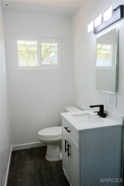 half bath featuring baseboards, vanity, and toilet