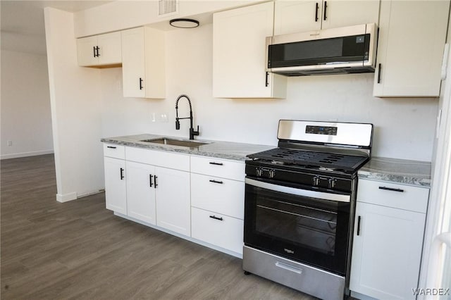 kitchen with appliances with stainless steel finishes, wood finished floors, a sink, and white cabinetry
