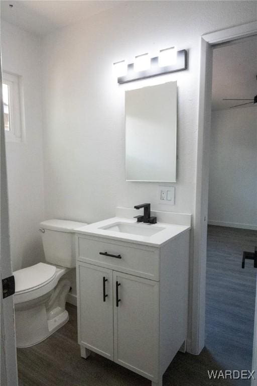 half bath featuring wood finished floors, toilet, vanity, a ceiling fan, and baseboards