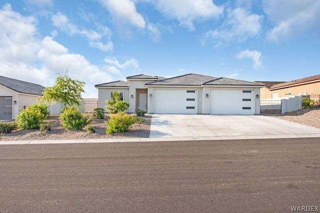 prairie-style home with an attached garage, fence, concrete driveway, and stucco siding